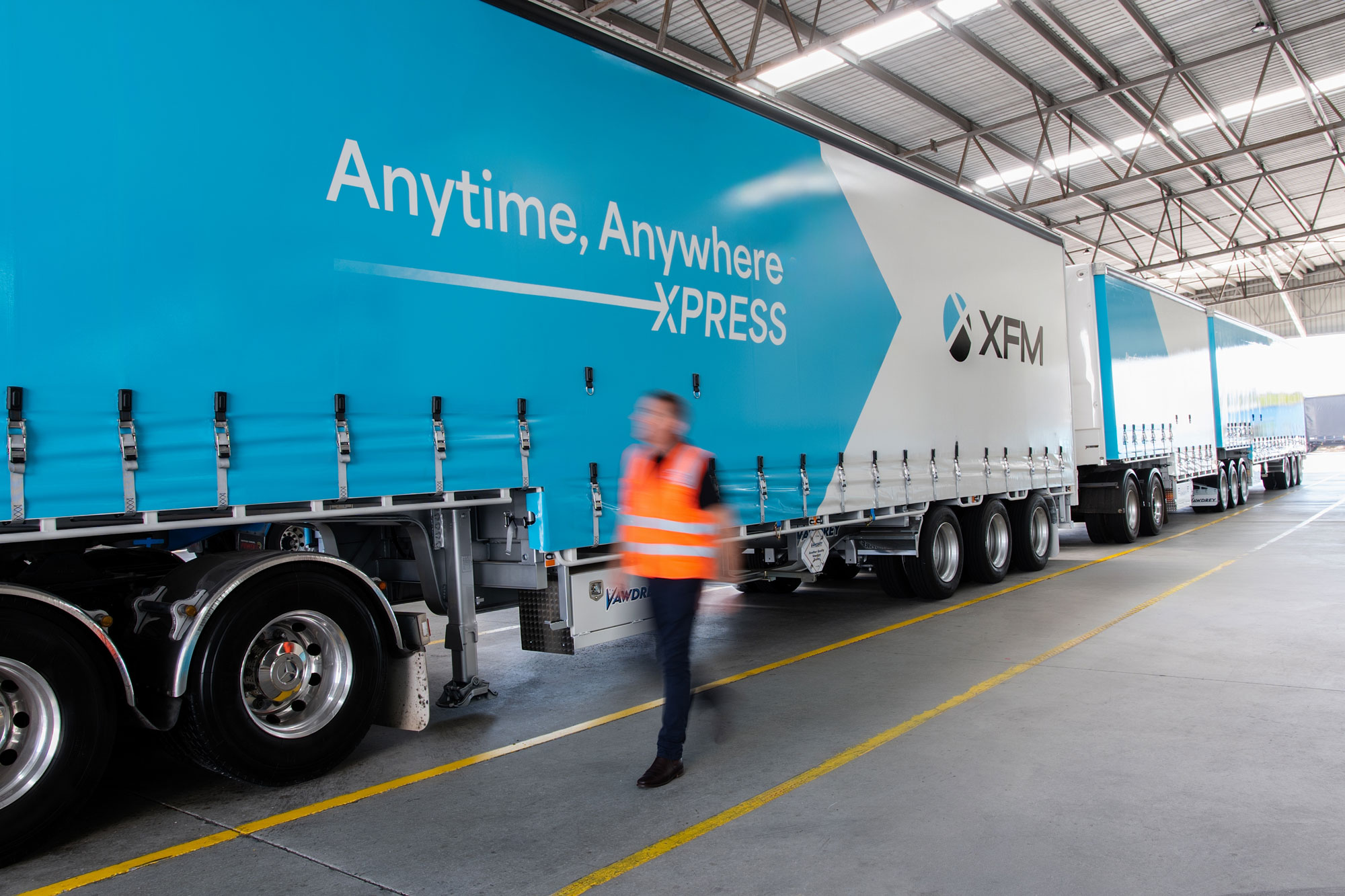 XFM employee walking beside a freight truck at a transport depot.