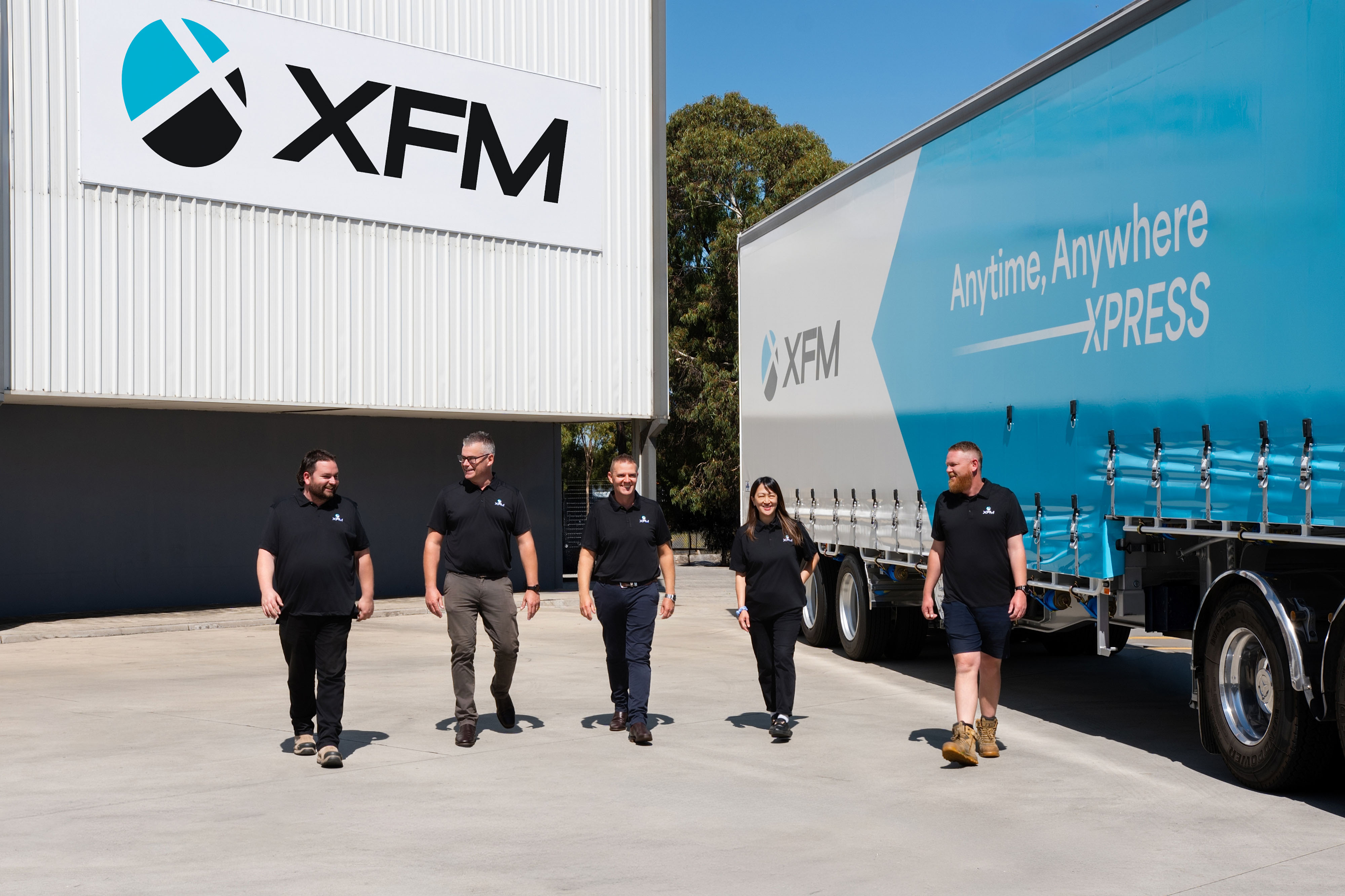 XFM freight and logistics team standing beside company trucks at an Australian transport depot.